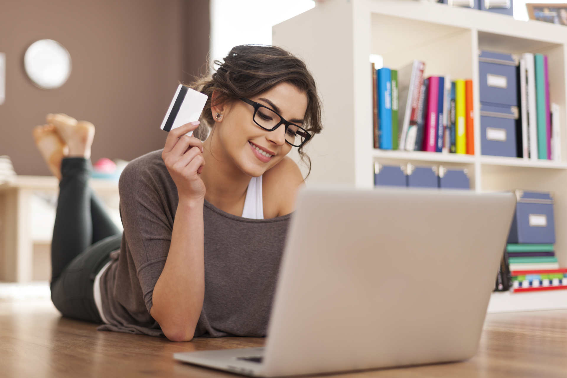 Frau liegt am Boden am Online shoppen mit Kreditkarte in der Hand